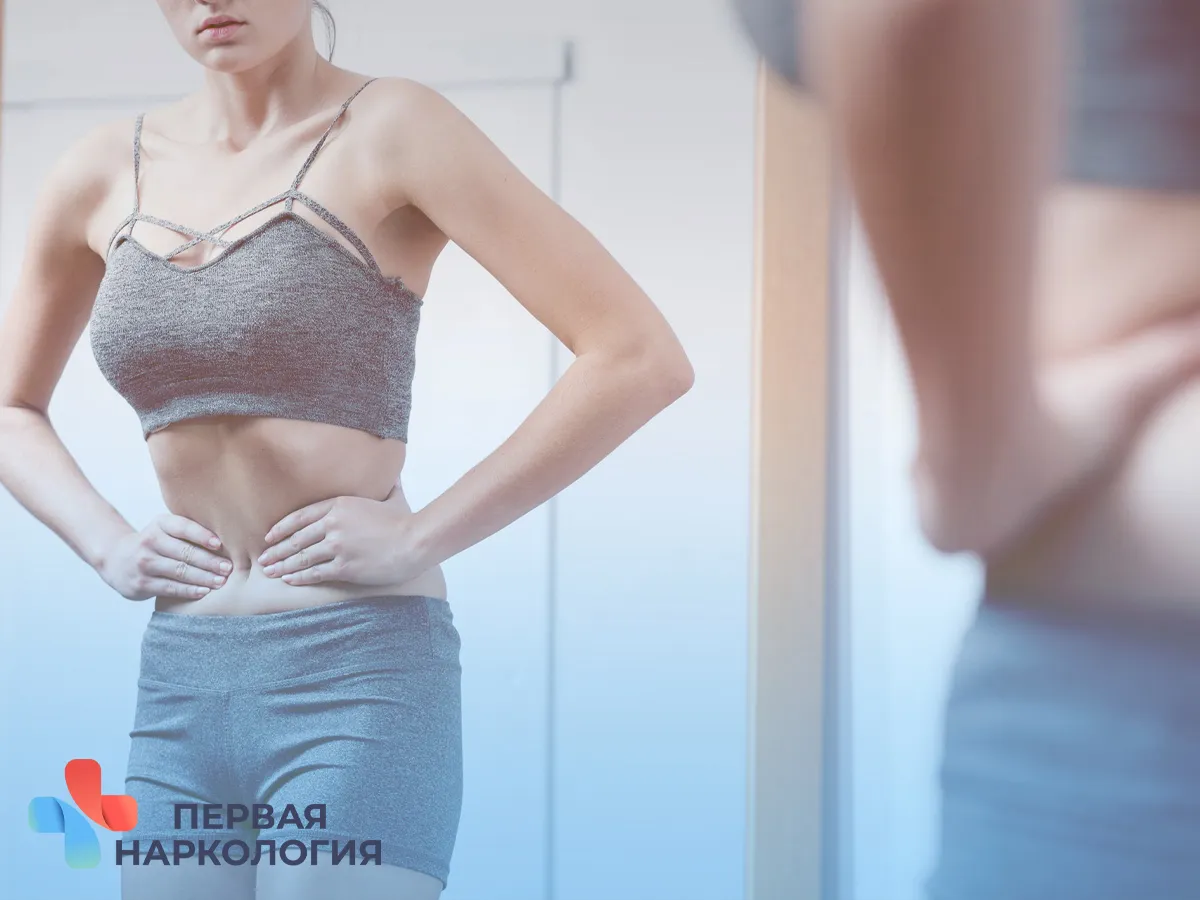 Девушка пытается ужать свою талию перед зеркалом